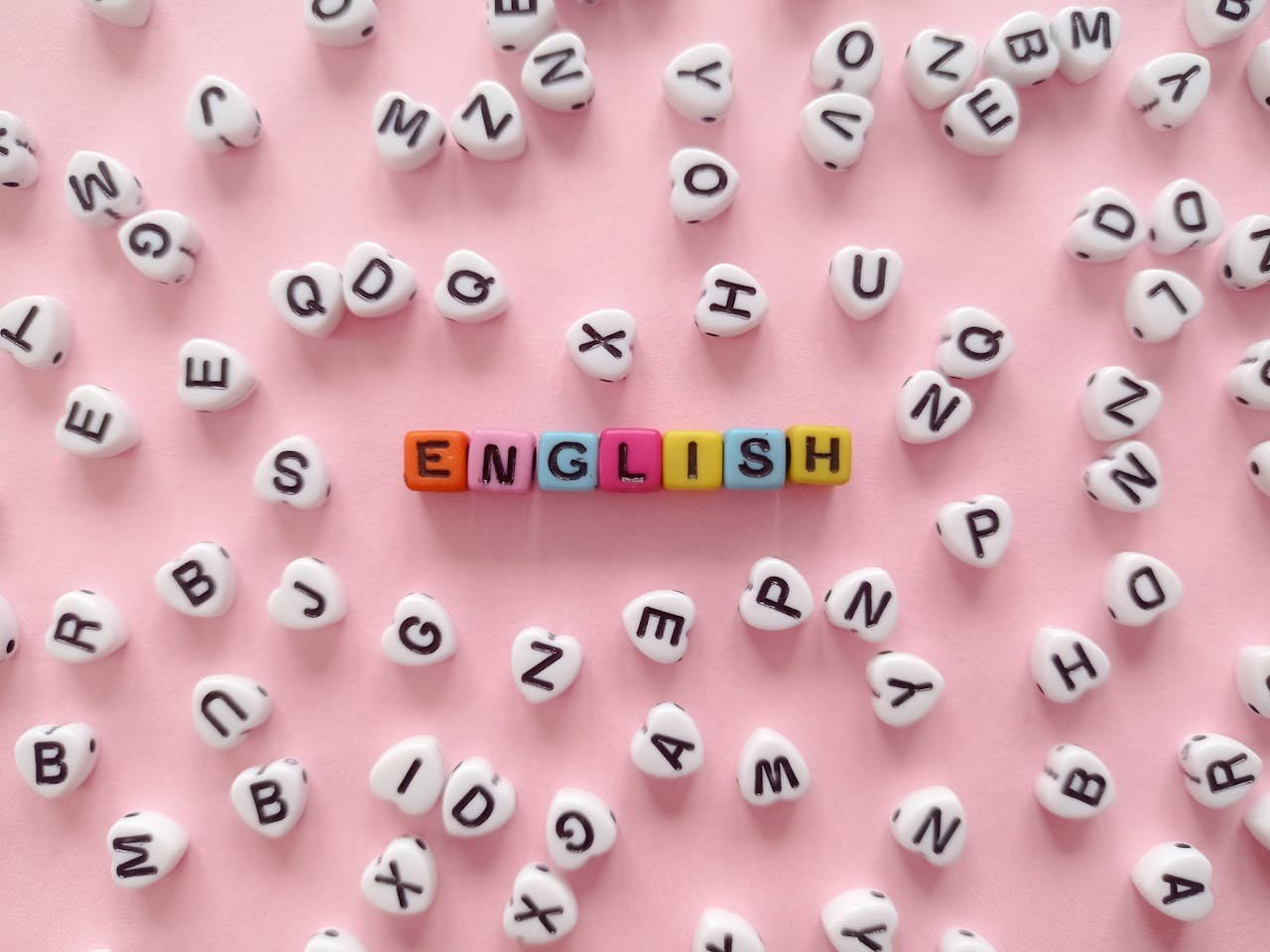 Scattered letter beads form the word English on a pink background, symbolizing language learning.